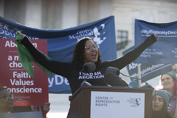 Bracey Sherman stands at a podium with her arms in the air, wearing a shirt that reads &quot;I had an abortion&quot;