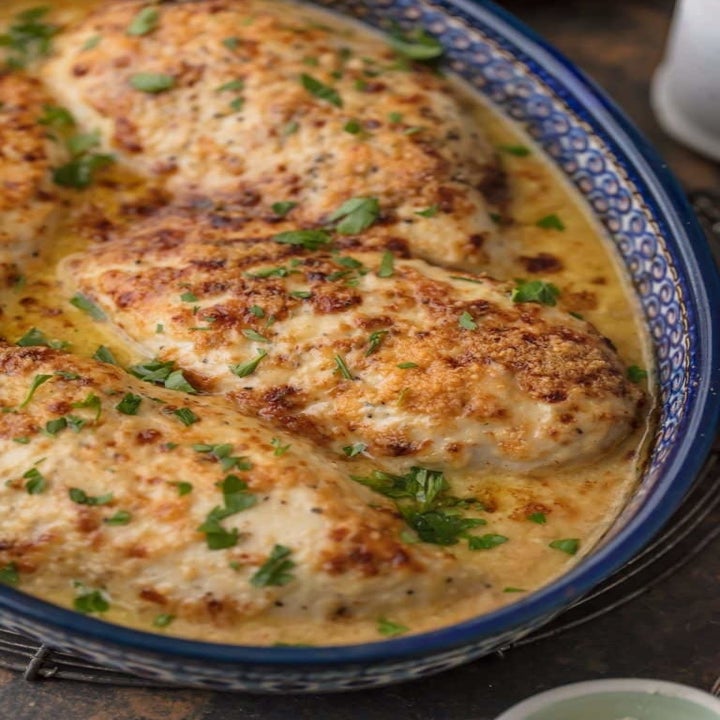 A dish filled with three pieces of chicken in Caesar sauce.