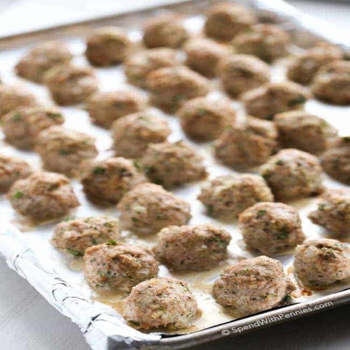 Dozens of meatballs lined up on a baking sheet.