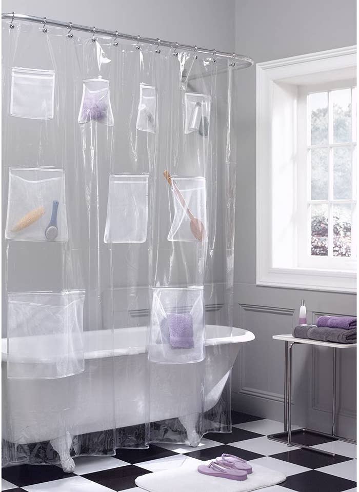 A plastic shower curtain with nine pockets on it The pockets are different sizes and have different items like a loofah, beauty products or towels inside.
