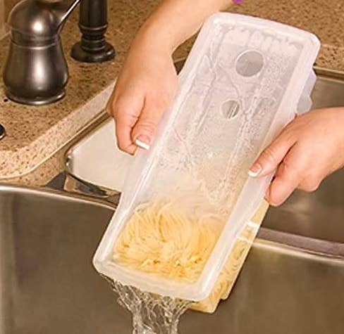 Hands drain water out of a clear container filled with cooked pasta