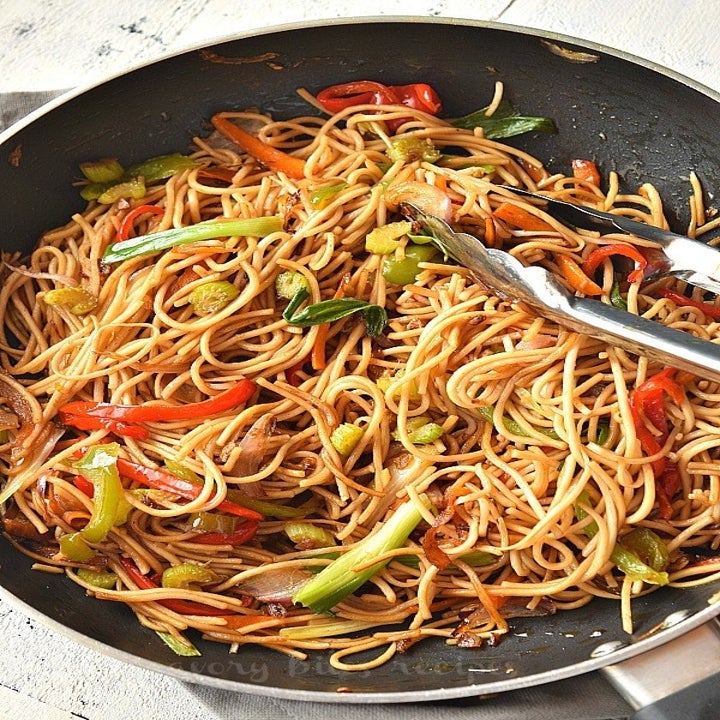 A skillet with lo mein noodles, thinly sliced peppers, carrots, and scallions.
