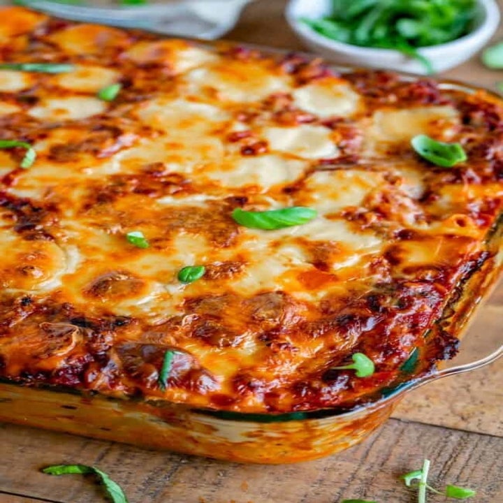 A baking dish filled with cheesy baked ziti in marinara sauce with fresh herbs.