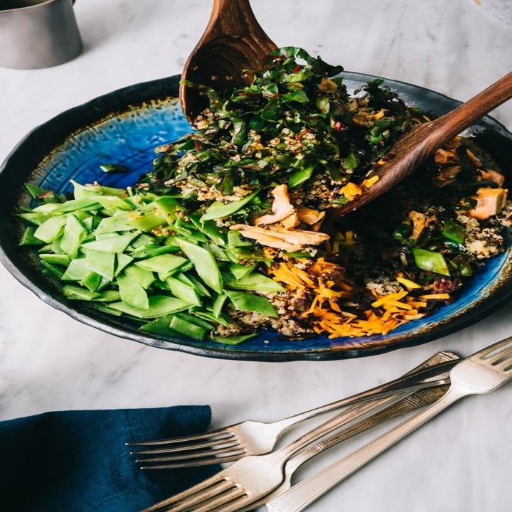Quinoa, sliced salmon, chopped snap peas, shredded carrots, and chard being tossed in a bowl.