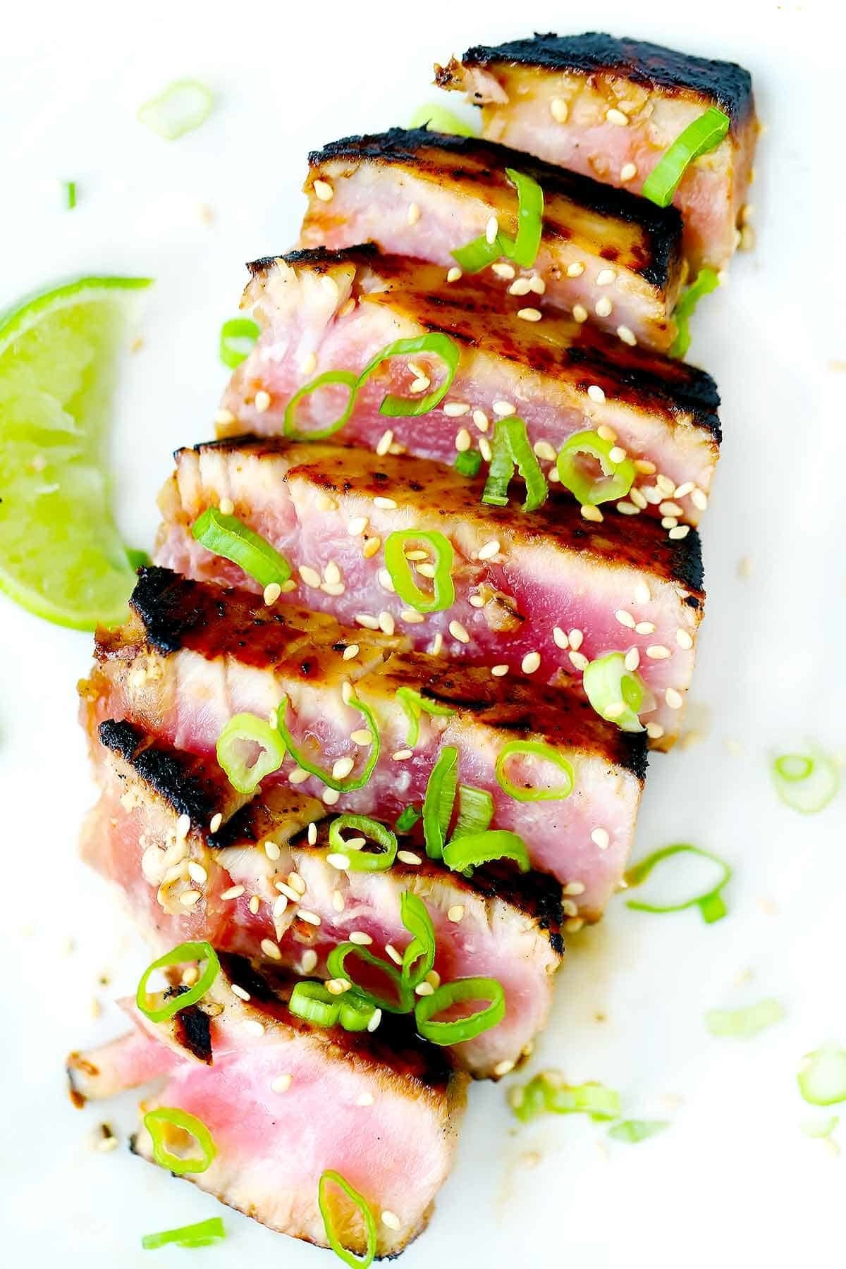 An ahi tuna steak, seared and rare on the inside, sliced into strips and topped with scallions and sesame seeds.