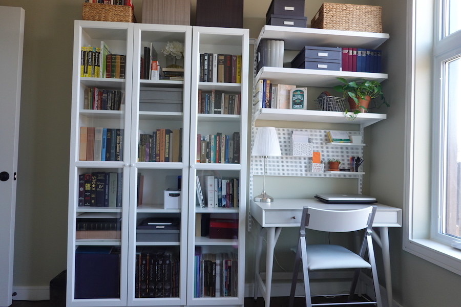 A small desk under three shelves and next to a bookcase with glass doors