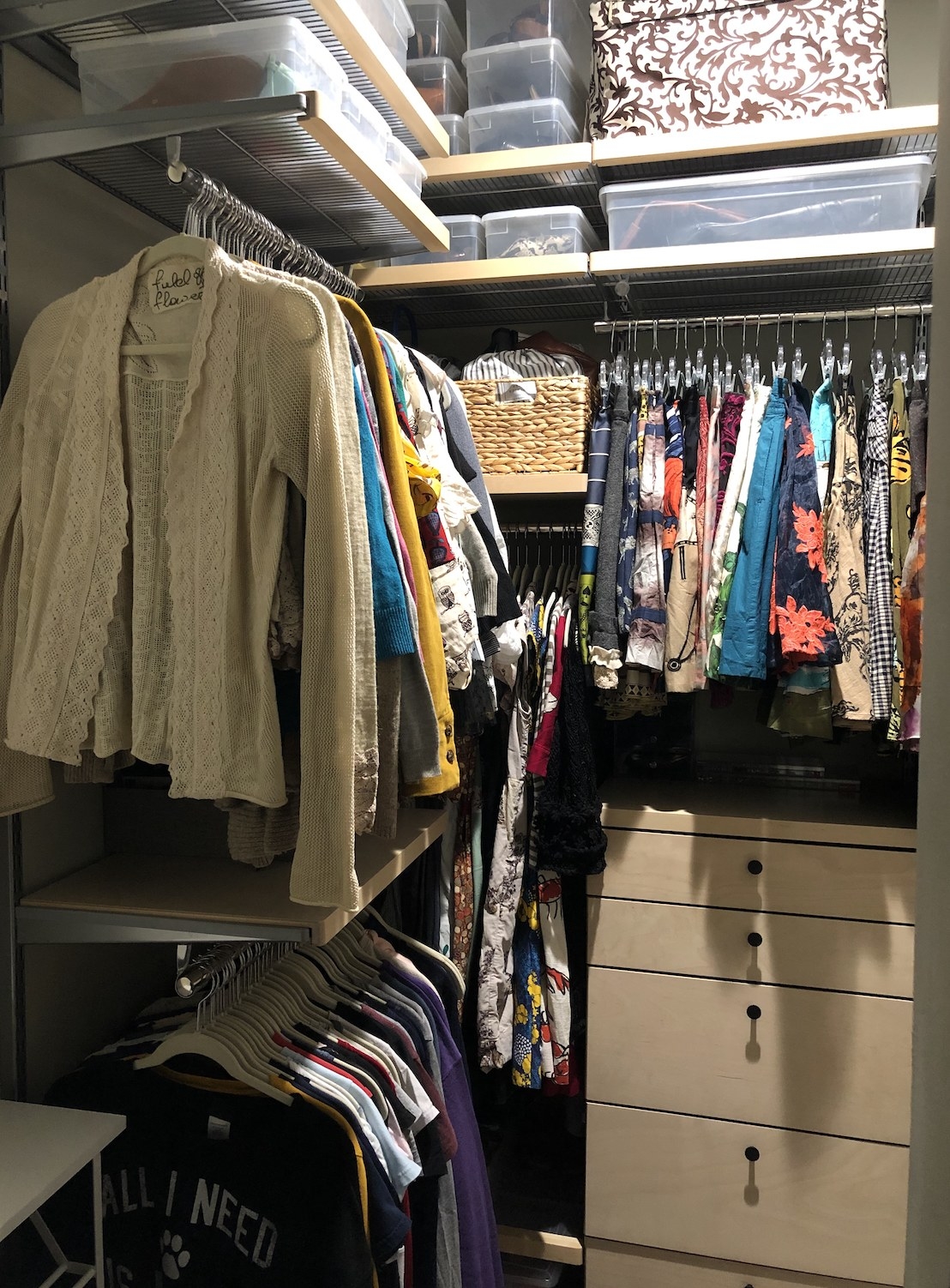 A corner closet with four short hanging rods, a chest of drawers, and several shelves holding boxes, bins, and baskets