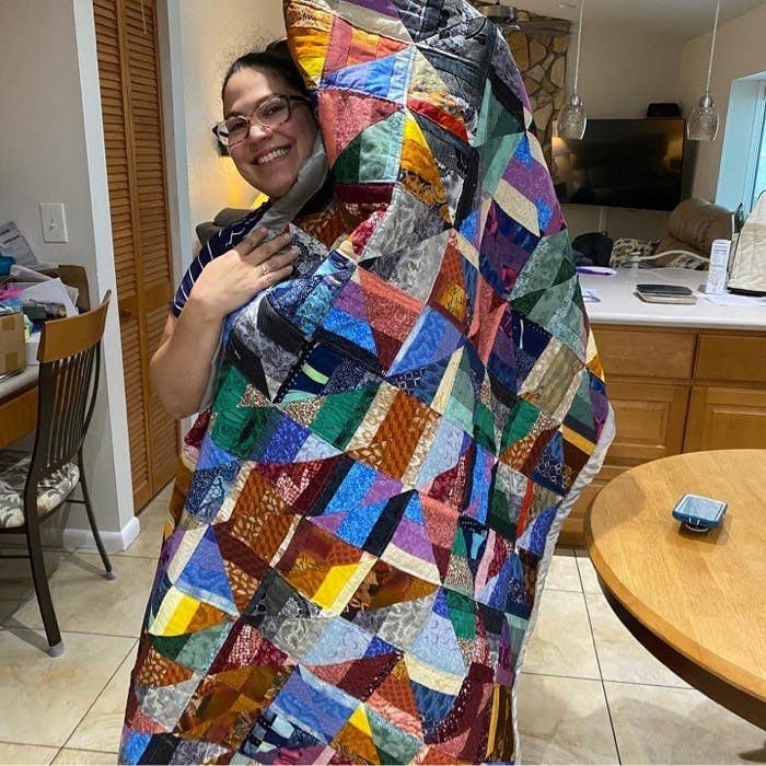 A woman proudly holding up a patchwork quilt that&#x27;s bigger than she is