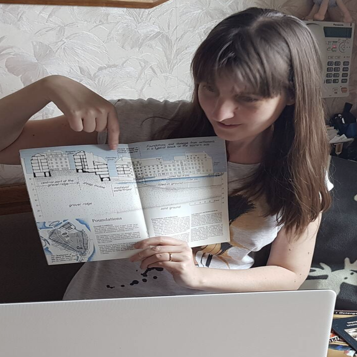 A woman holds up an informative booklet to a computer, pointing towards it