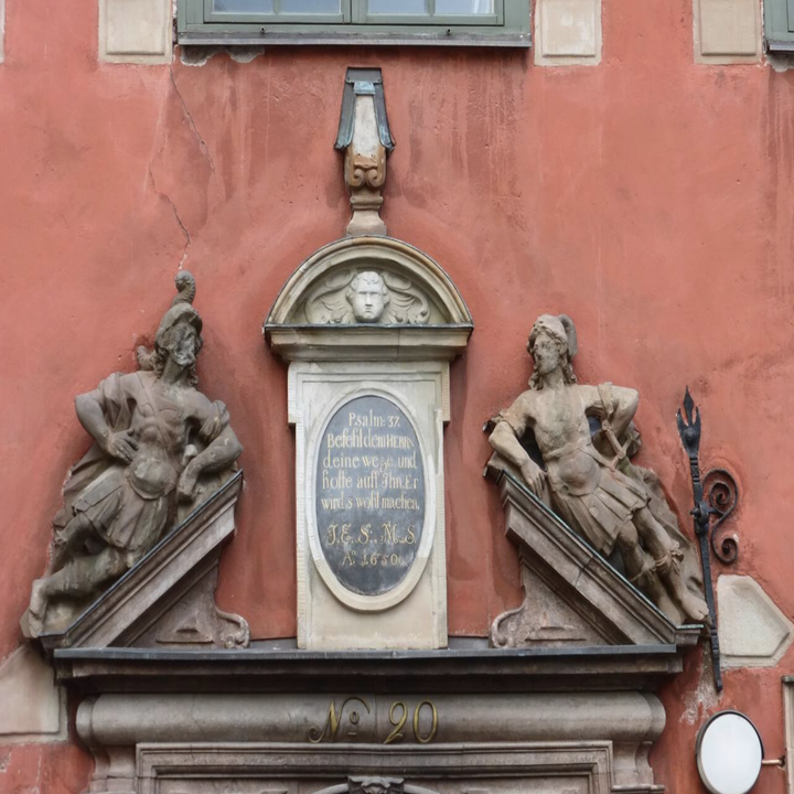 A close up of a historic building's plaque in Swedish, two statues resting beside it