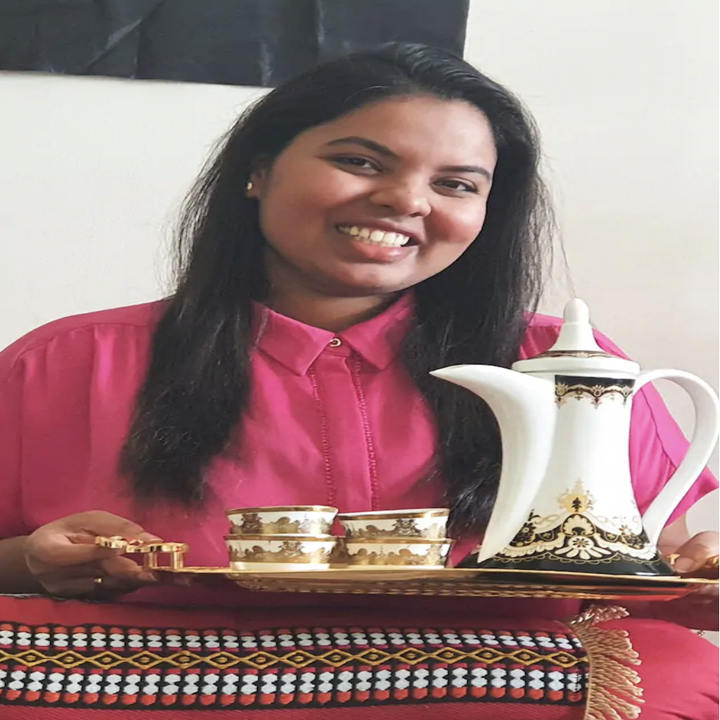 A woman smiles and holds up a tray with traditional coffee cups and pot