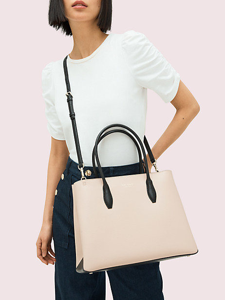 A model with a beige satchel with black straps hanging from their shoulder