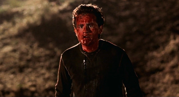 A man's face is covered in blood, he looks at something off camera in disgust