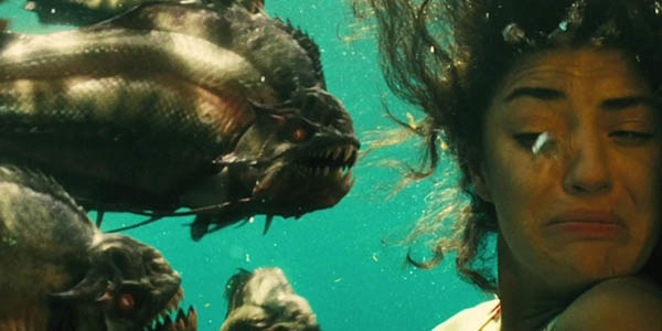 A woman is underwater with at least three huge piranhas right in front of her face, she turns away from them in fear