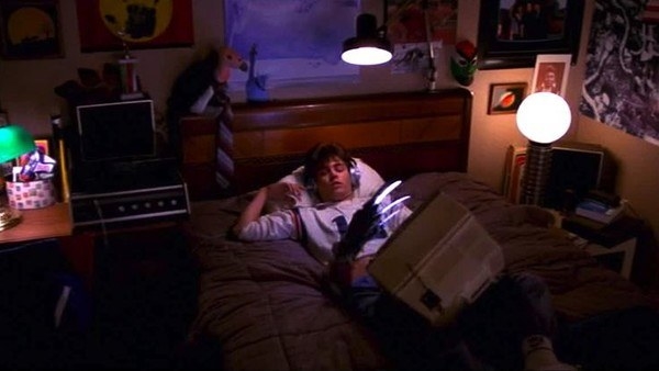 A teenage boy sleeps on his bed while a clawed hand rises up from inside the bed, reaching to grab him