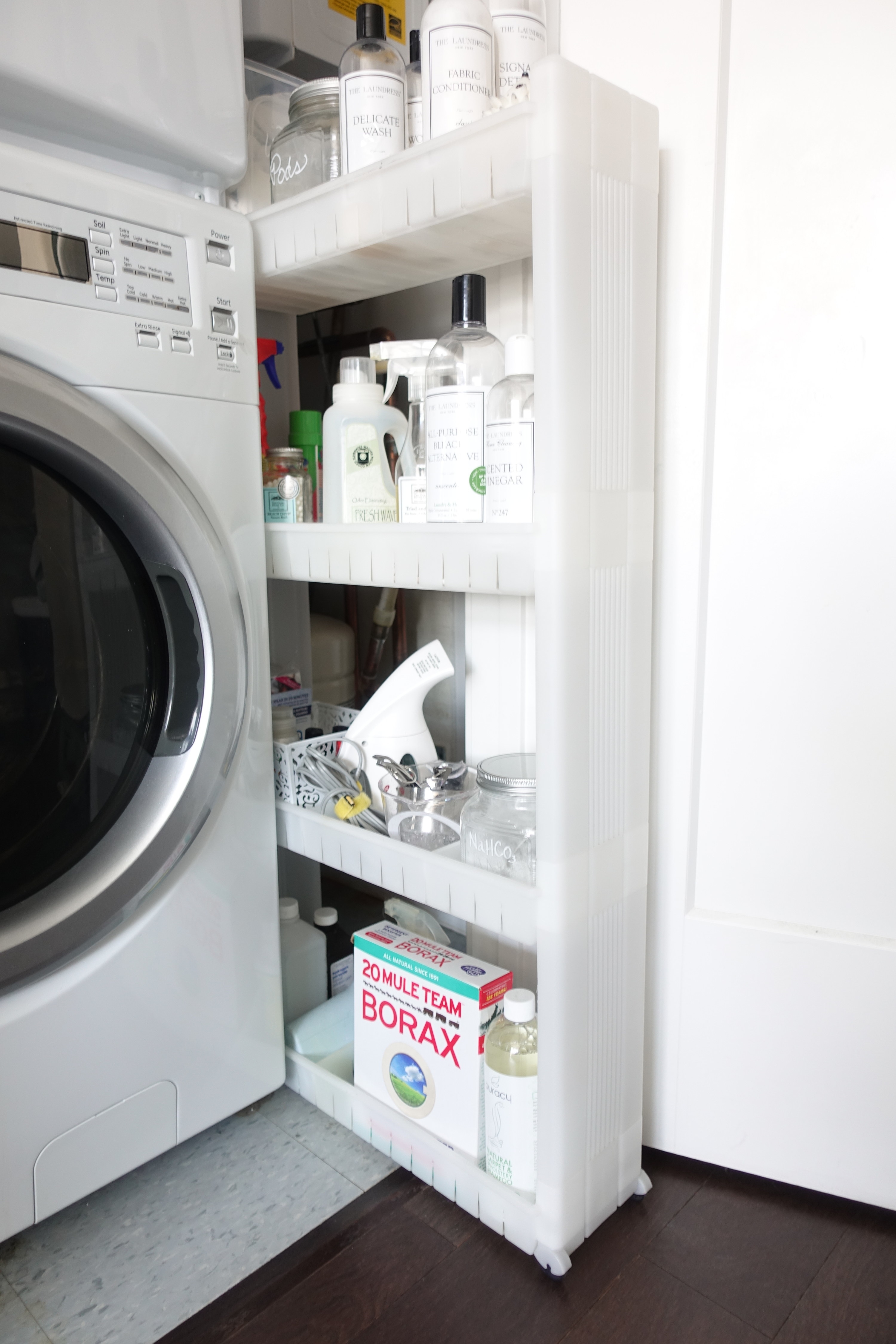 A skinny rolling cart holding laundry supplies next to a washing machine