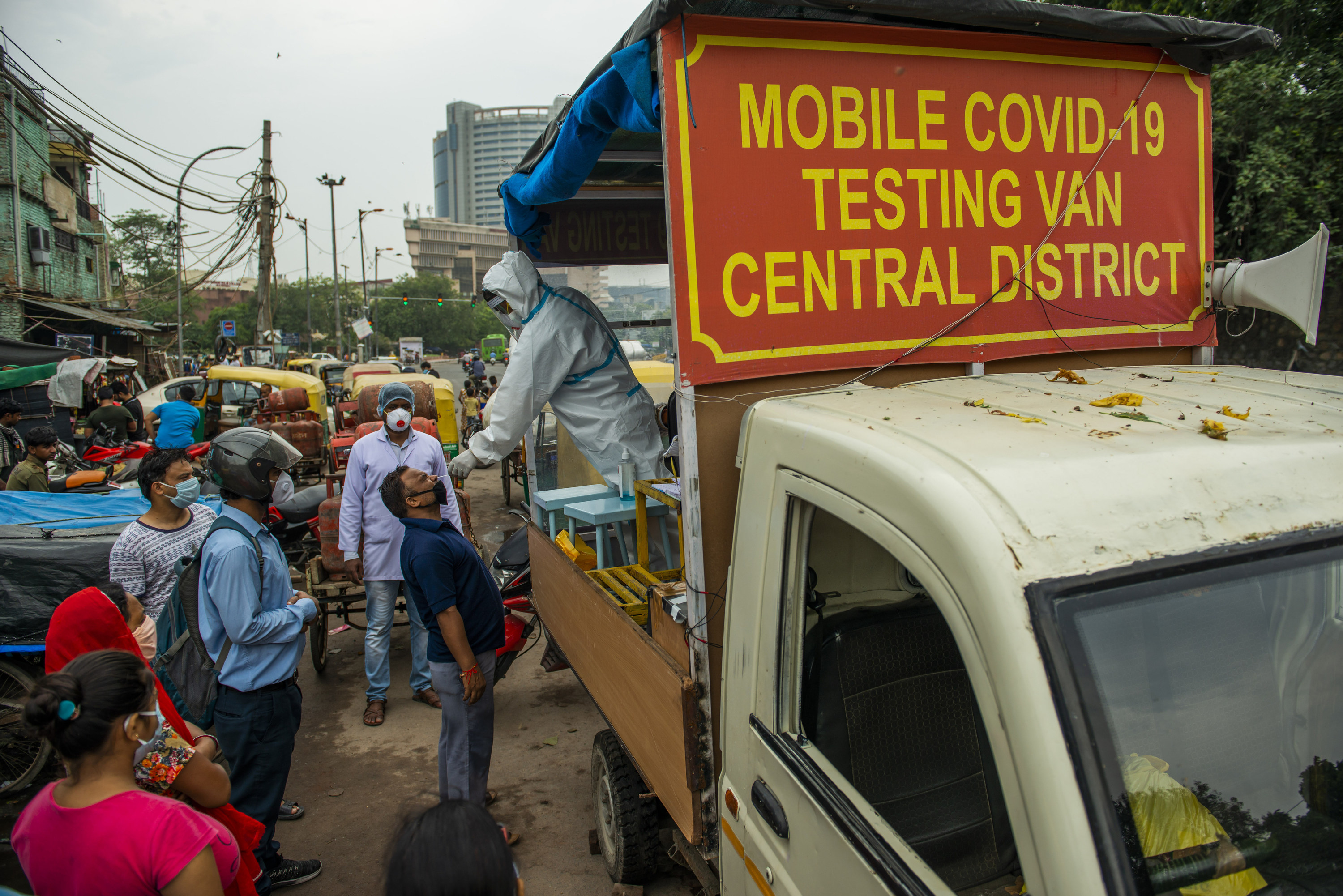 A man stands in the bed of a pickup truck that reads &quot;Mobile COVID-19 Testing Van Central District,&quot; while administering a nasal swab