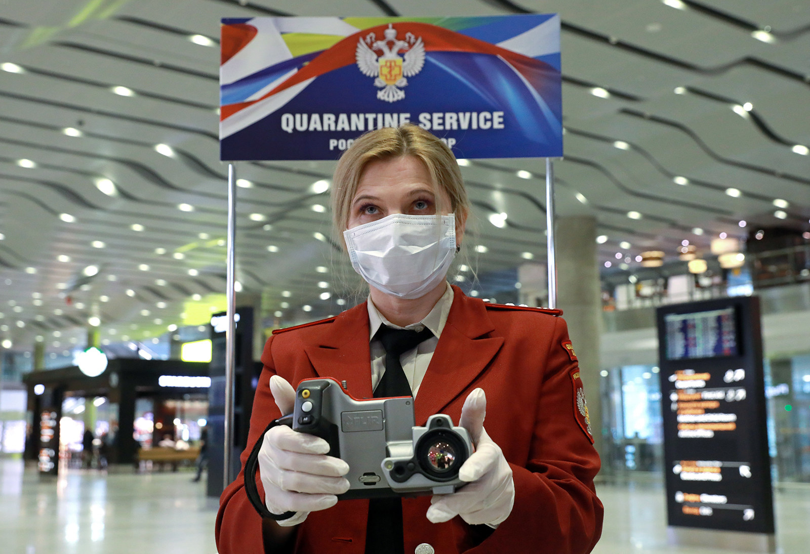 A woman wearing a facemask and white gloves holding a camera