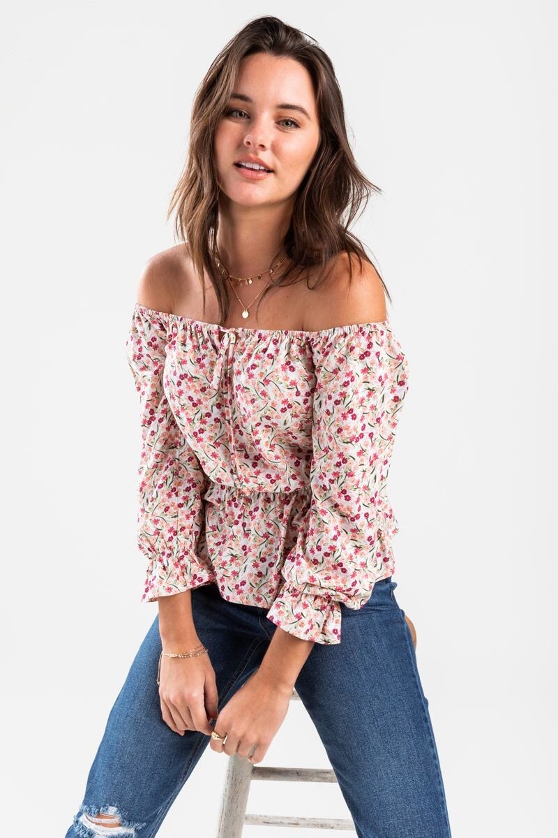 a model sitting on a stool in jeans and the peasant top which is light pink and covered in tiny pink and yellow florals