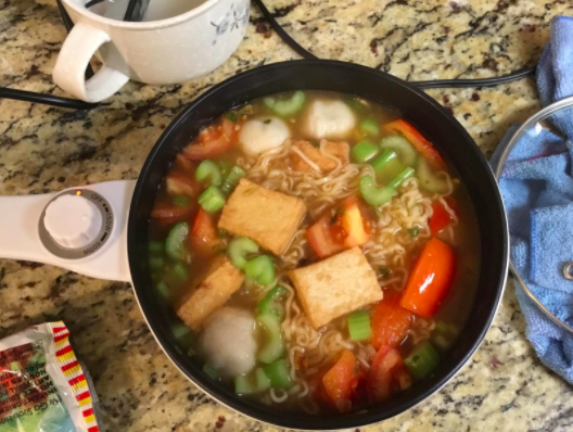 Reviewer&#x27;s white electric hot pot filled with ramen noodles, veggies, and tofu
