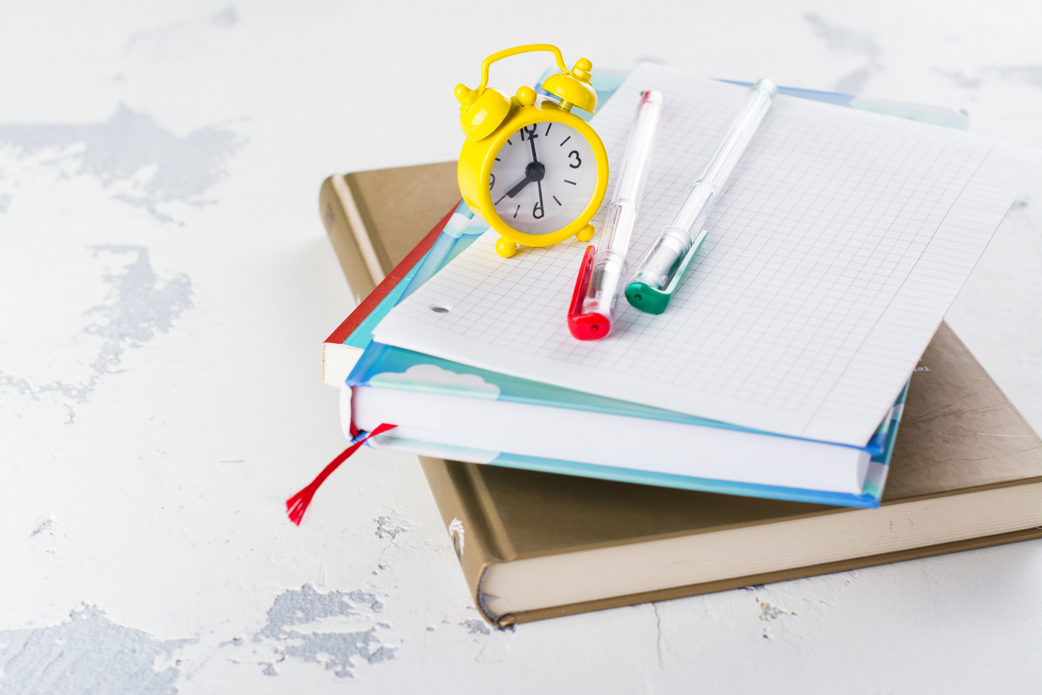 A stack of books and homework with an alarm clock on top