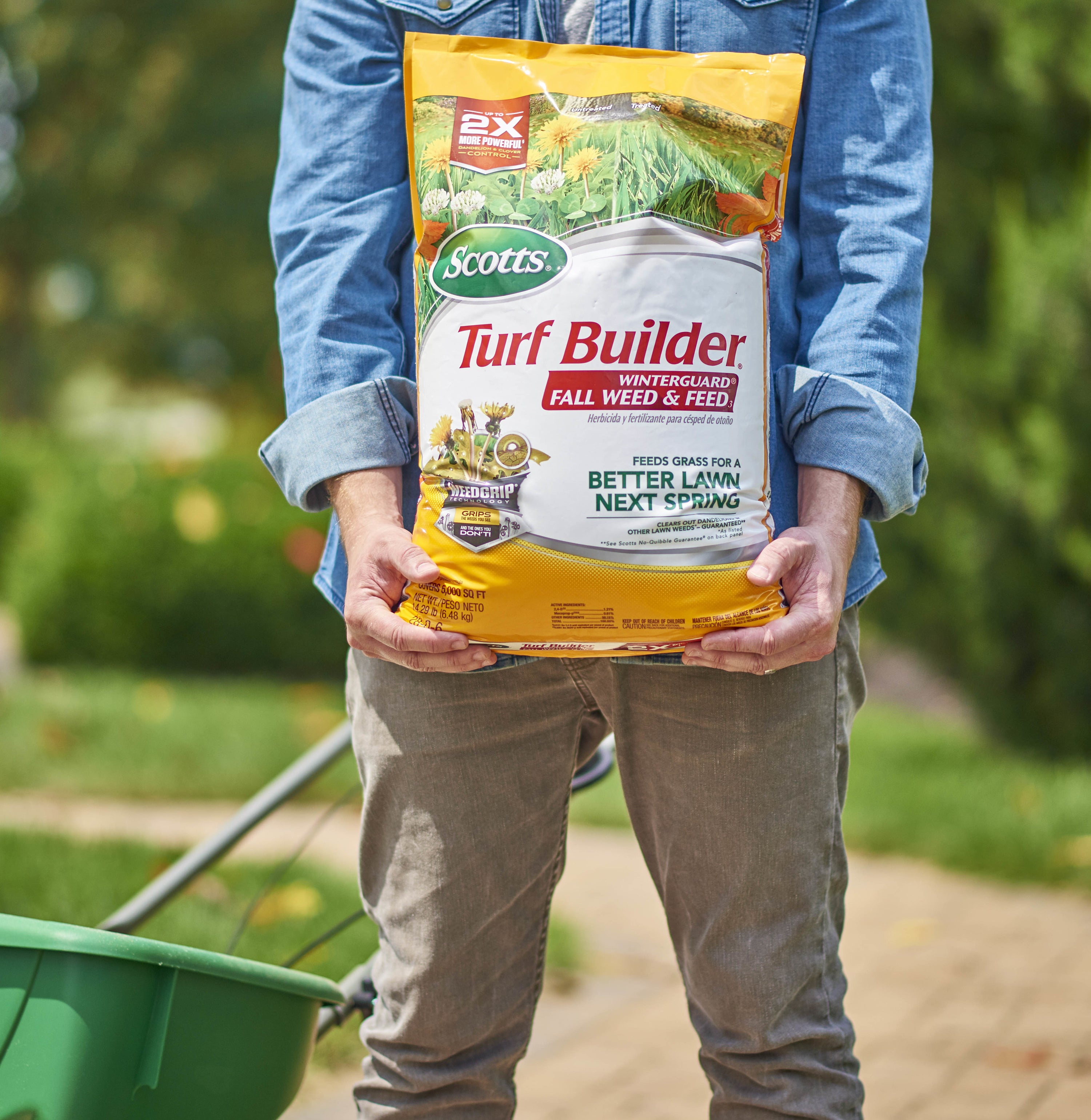 Model holding a large yellow bag of Scotts turf builder