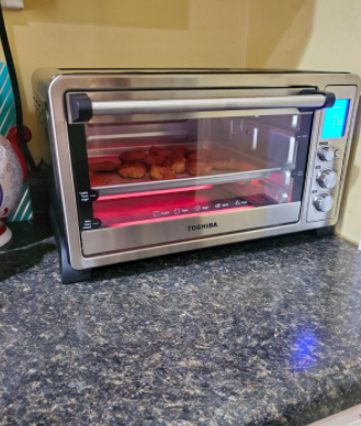 Reviewer cooks chicken nuggets in a silver digital toaster oven on their countertop
