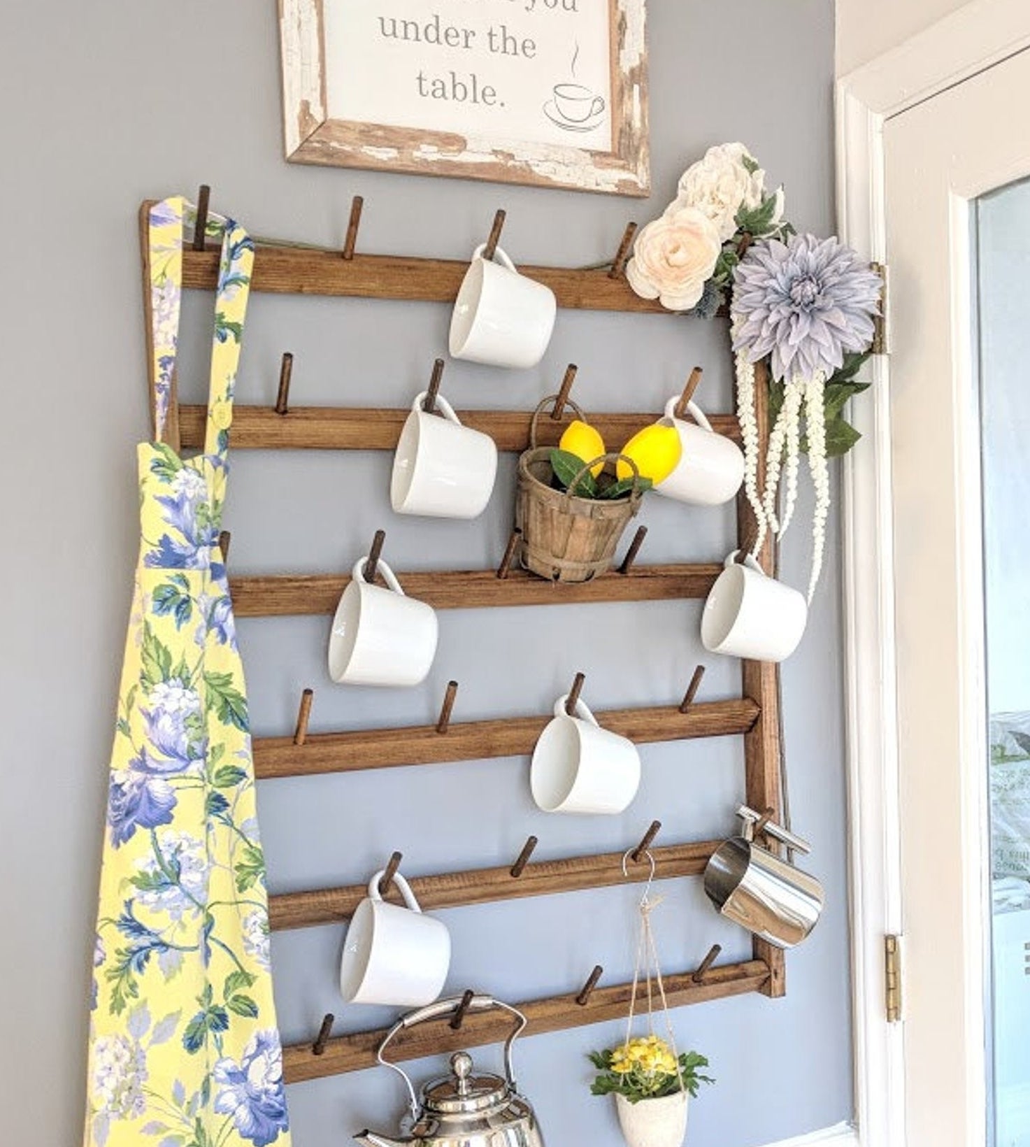 wood mug rack on wall holding many mugs and a kettle on its dowels