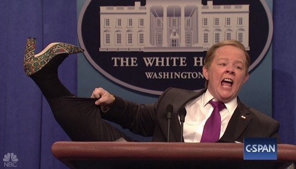 Melissa McCarthy as Sean Spicer, lifting her leg to show off a shoe