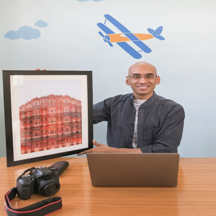 A man smiles and poses with a framed photo of Jaipur's famous pink building