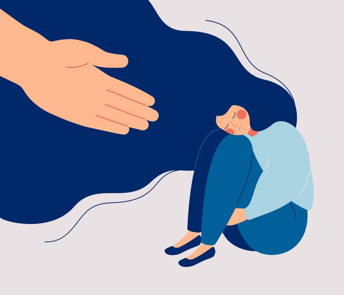 Cartoon woman sits alone with her head resting on her knees, a giant hand reaches down to symbolise a friend offering help or comfort