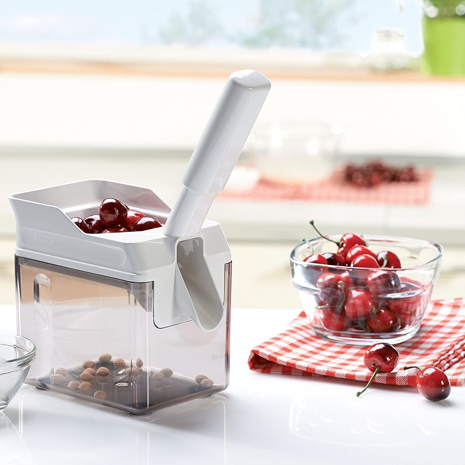 The cherry pitting machine on a kitchen counter next to a bowl of cherries