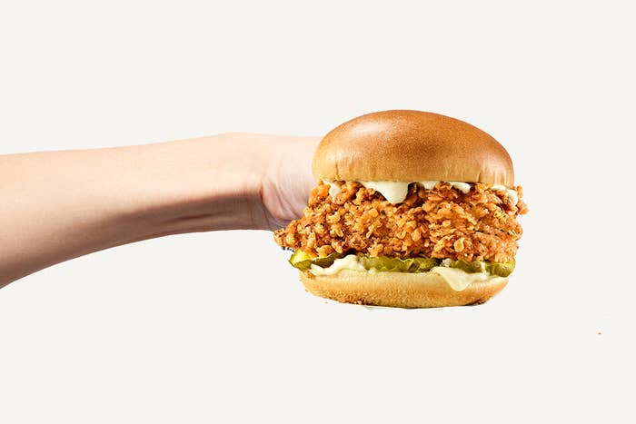 A hand on a white background throwing a punch where the fist is the Famous Chicken Chicken Sandwich.