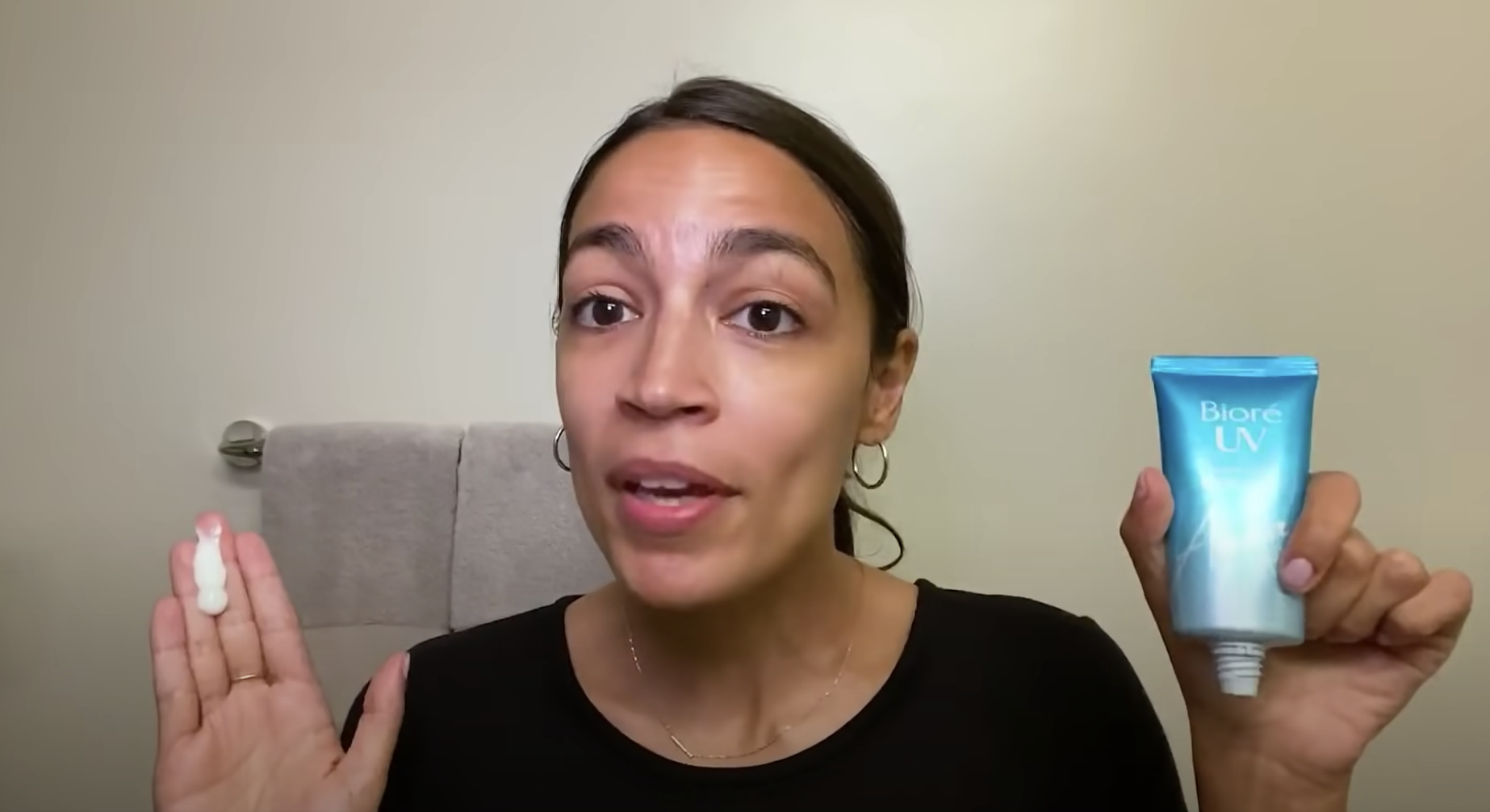 Alexandria Ocasio-Cortez talking to the camera and holding up a tube of sunscreen.