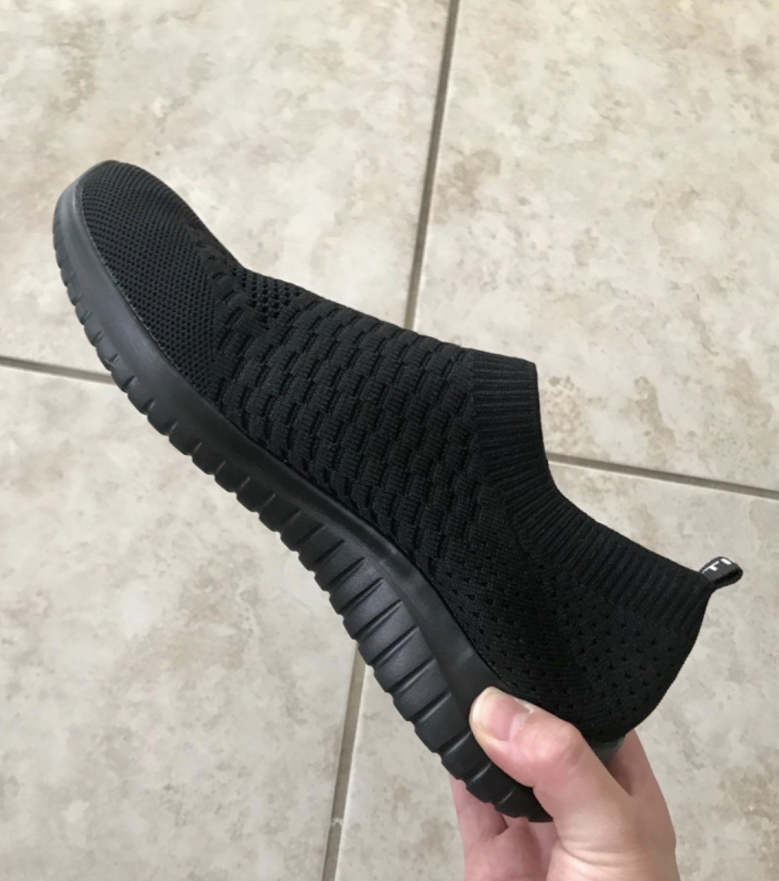 Reviewer holding the black sneaker with a sock and mesh-like material