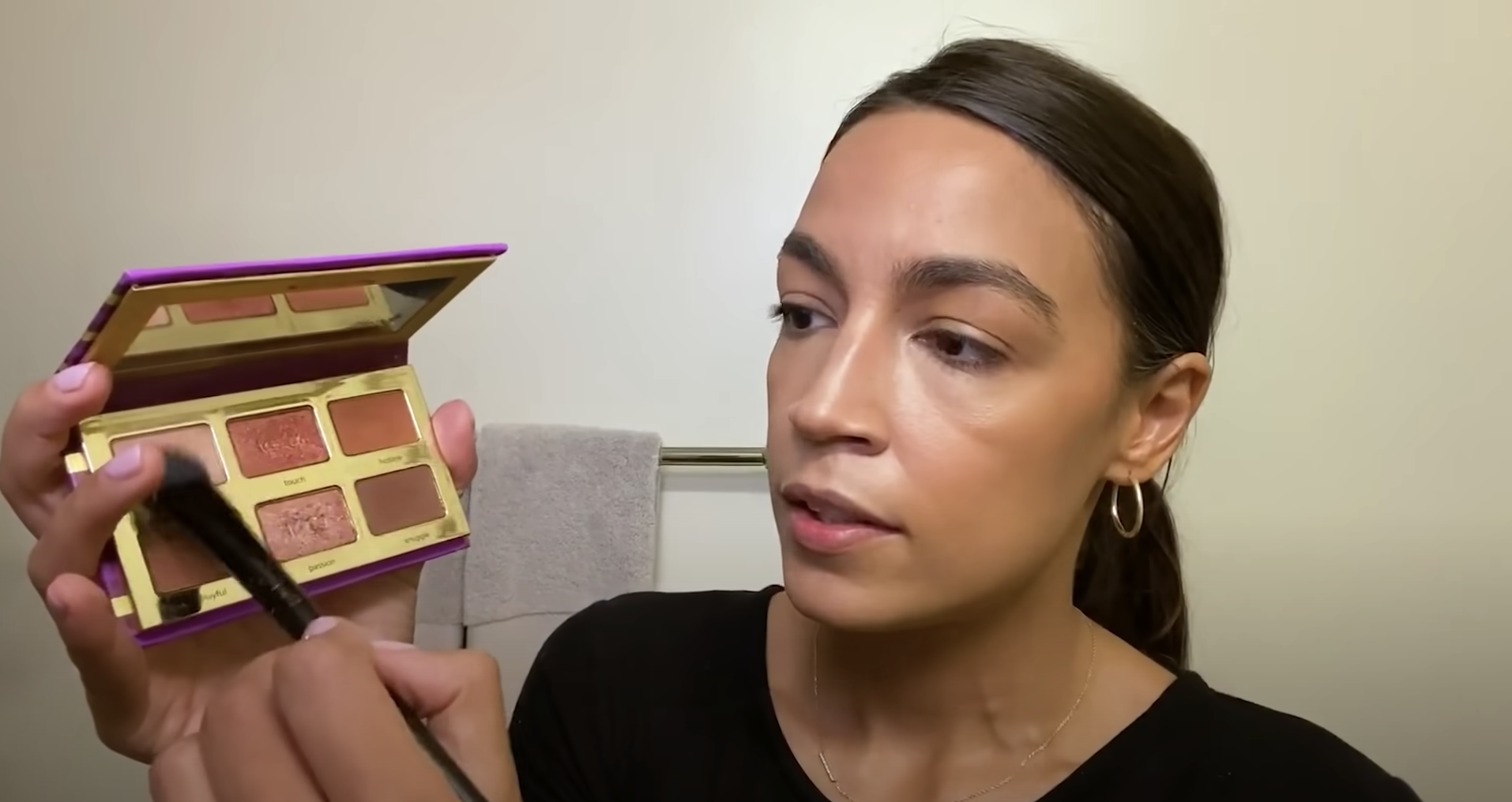 Alexandria Ocasio-Cortez applying eyeshadow from a palette.