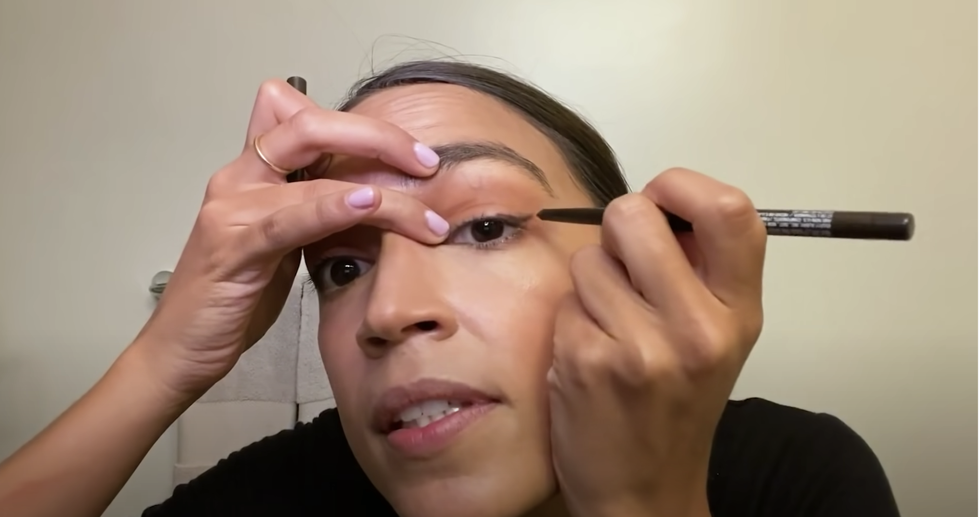 Alexandria Ocasio-Cortez applying eyeliner.