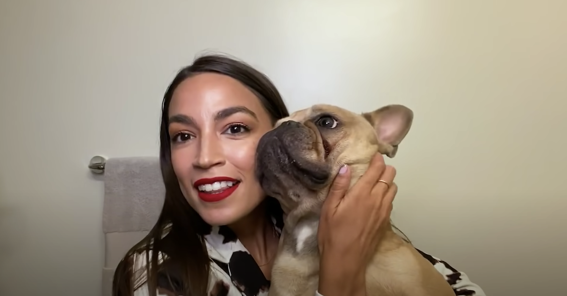 Alexandria Ocasio-Cortez smiling and holding her pet dog.