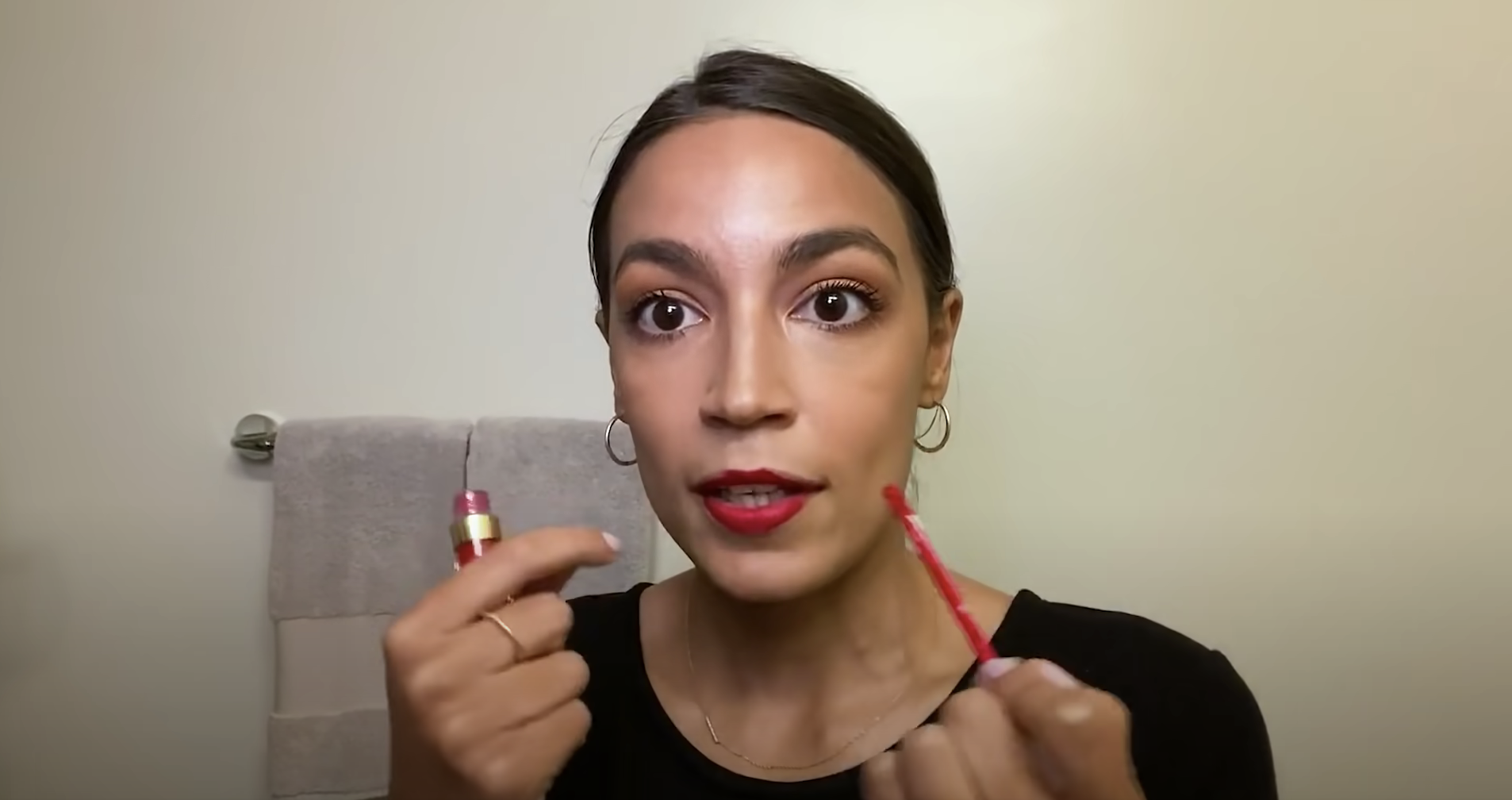 Alexandria Ocasio-Cortez applying red liquid lipstick.