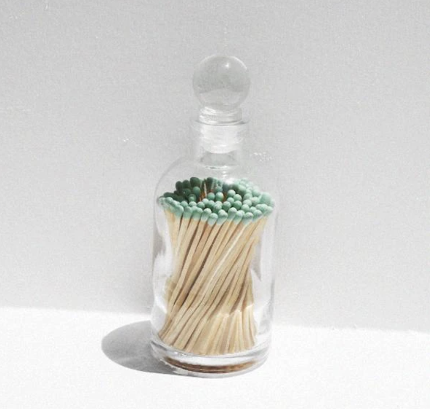 A clear glass case with matches inside with teal heads