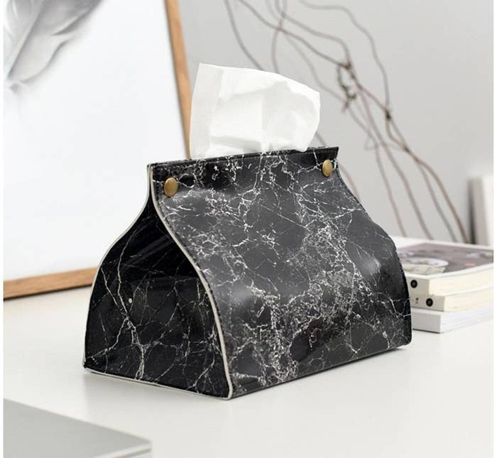 A black marble leather tissue box cover with gold hardware and a tissue coming out of the top
