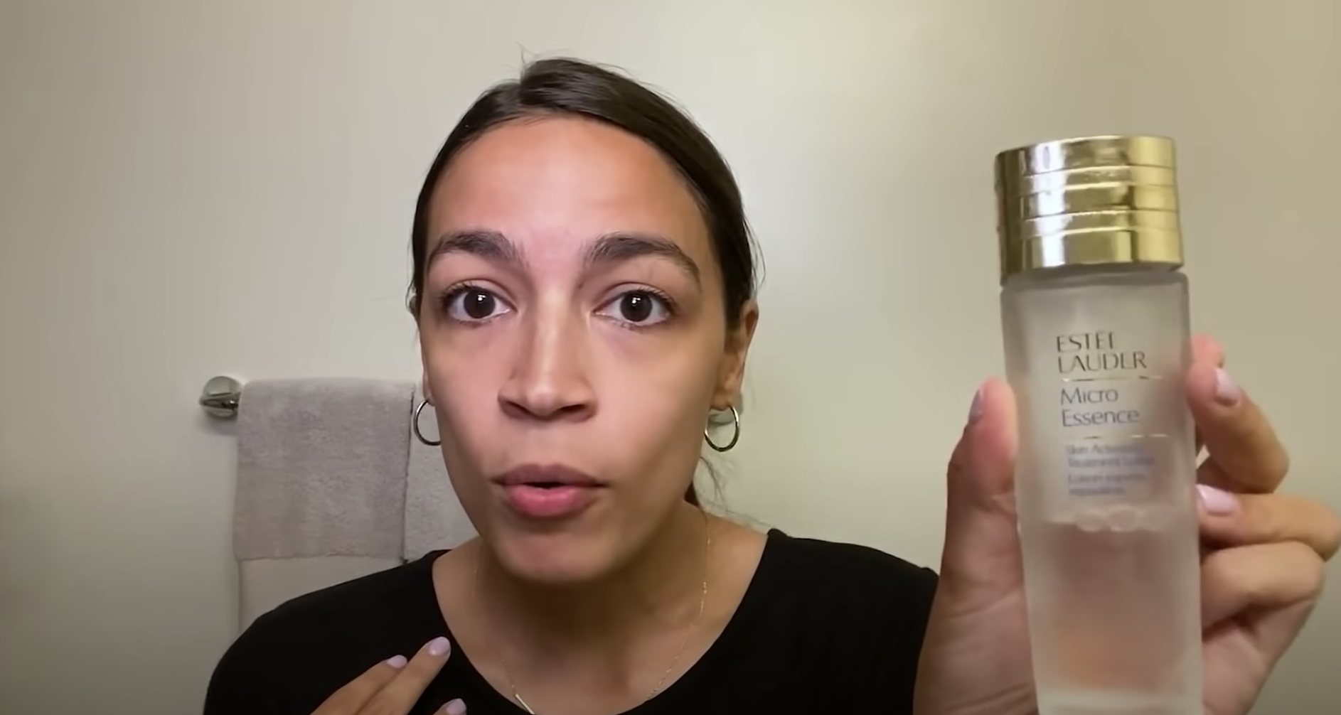 Alexandria Ocasio-Cortez talking to the camera and holding up a bottle of toner.
