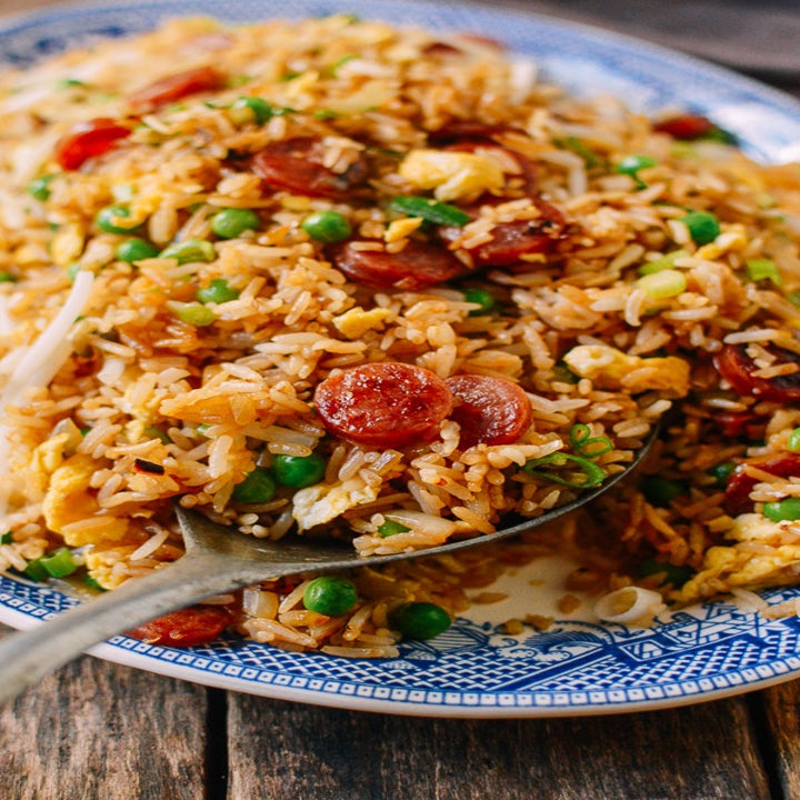 A spoon taking a scoop of sausage and pea fried rice.