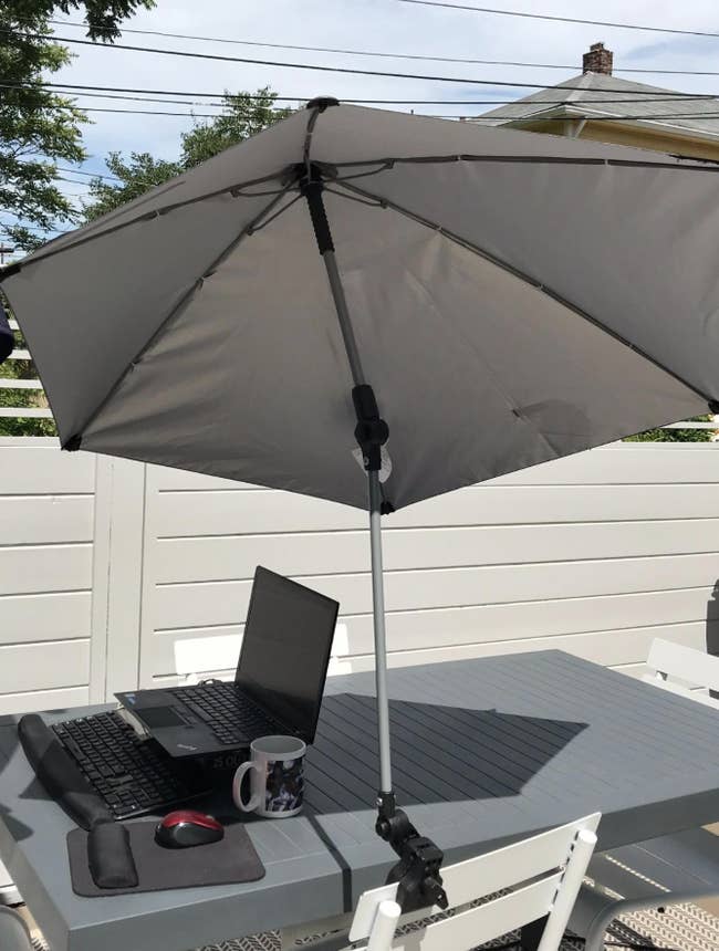 A white umbrella attached to a chair shading a laptop on a table