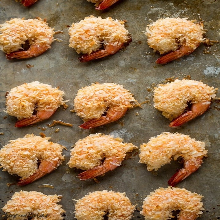 A dozen or so coconut crusted shrimp on a baking sheet.