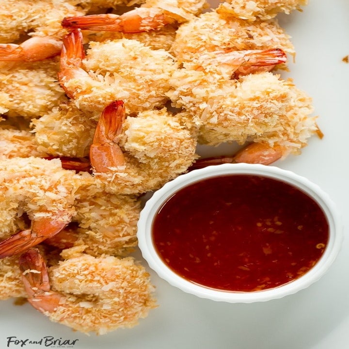 A handful of crispy coconut shrimp with a ramekin full of cocktail sauce.