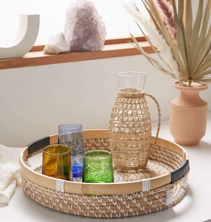 Woven seagrass serving tray with cutout side handles and assorted glasses in it