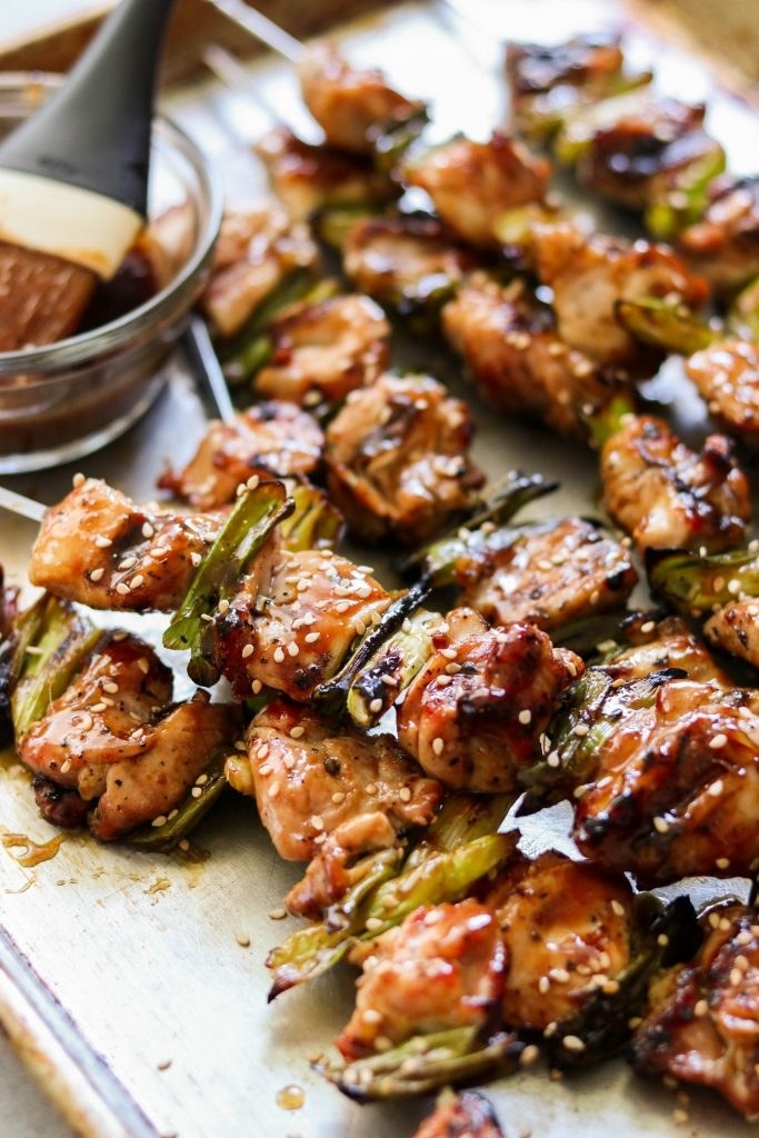 Skewers of chicken yakitori with scallions and sesame seeds on a baking sheet.
