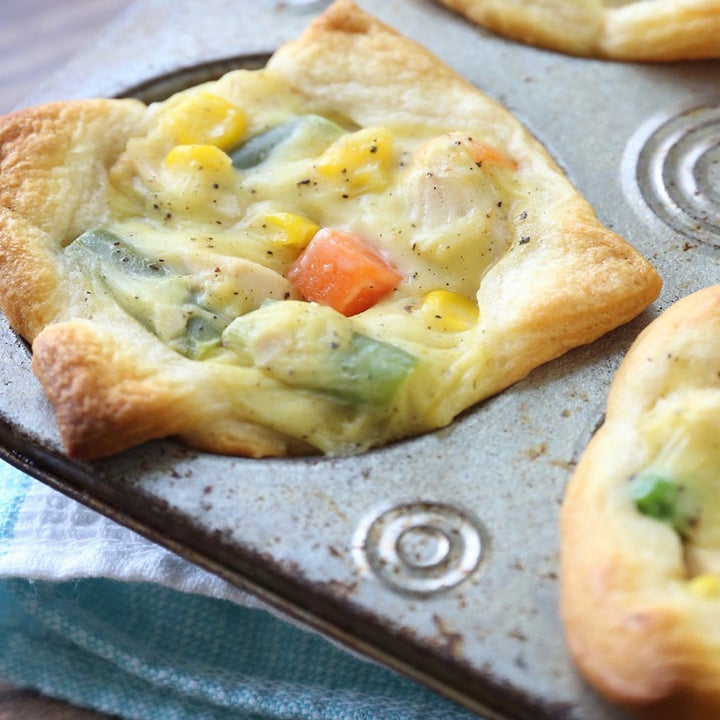 A muffin tin with a few chicken pot pies stuffed with chicken and veggies under crescent dough topping.