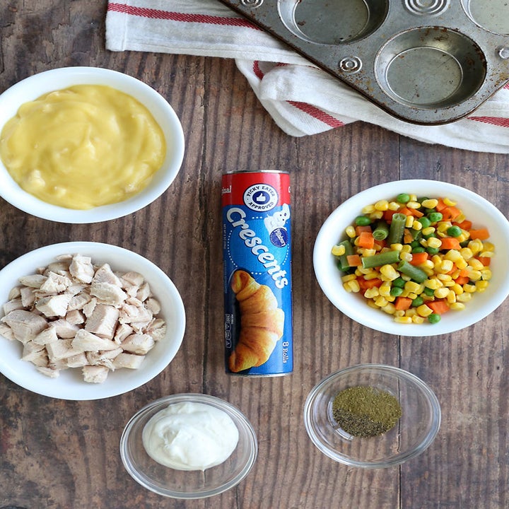 A tabletop with ingredients on top including cream of chicken soup, cooked, diced chicken, frozen vegetables, and crescent dough.